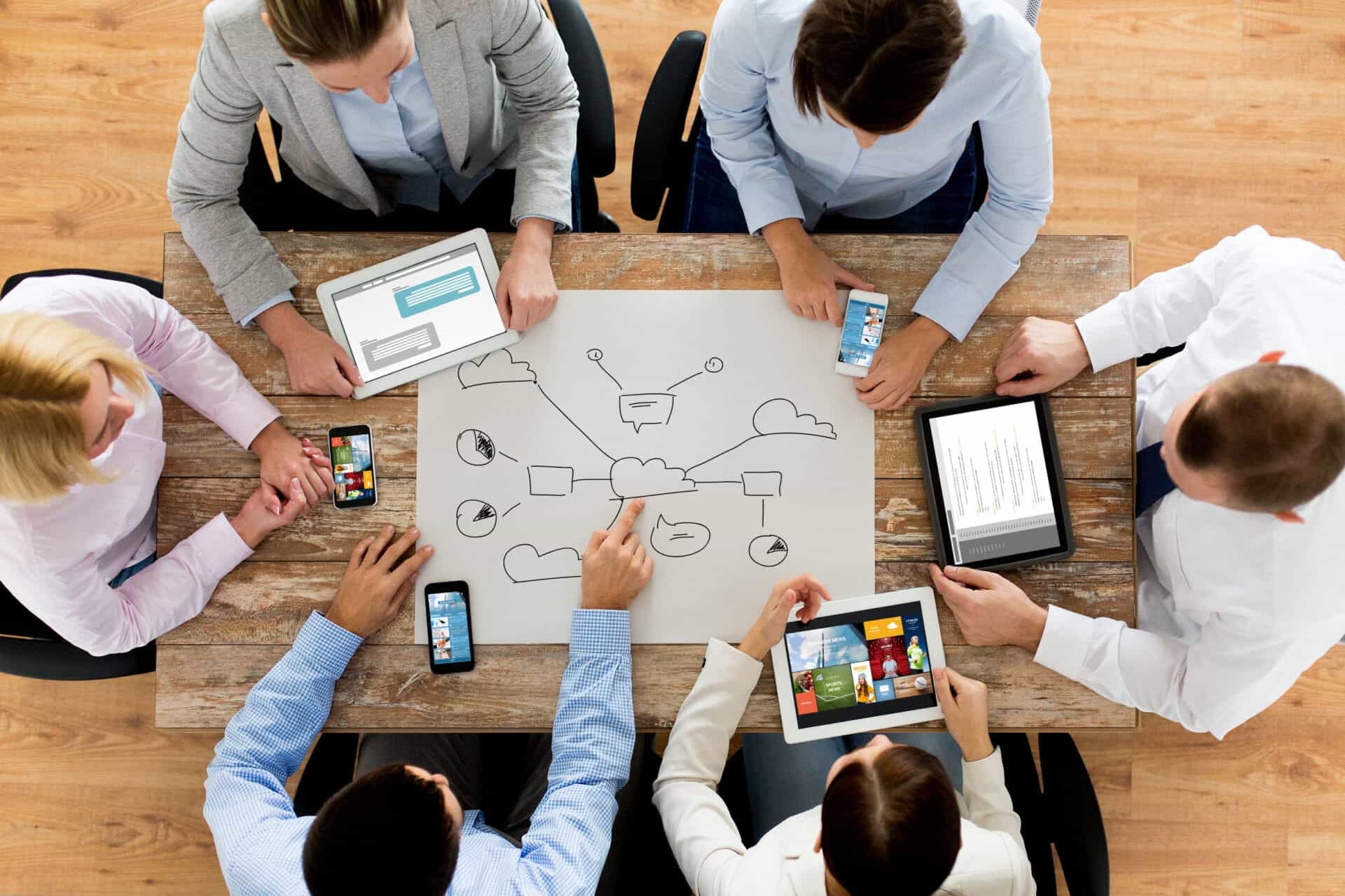 business, people, technology, cloud computing and team work concept - close up of creative team with smartphones and tablet pc computers sitting at table in office